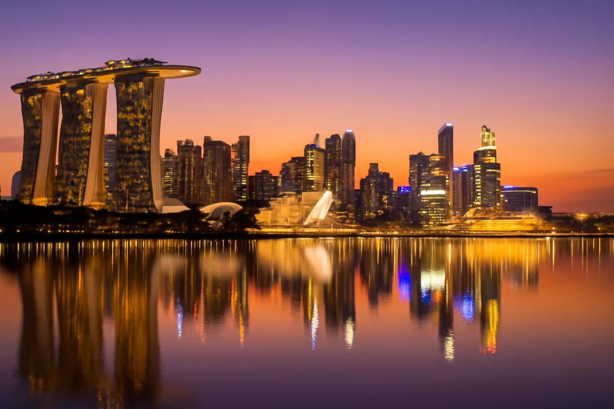 Singapore skyline at dusk with Marina Bay Sands resort and city lights reflecting on the calm waters of Marina Bay under a golden purple twilight sky